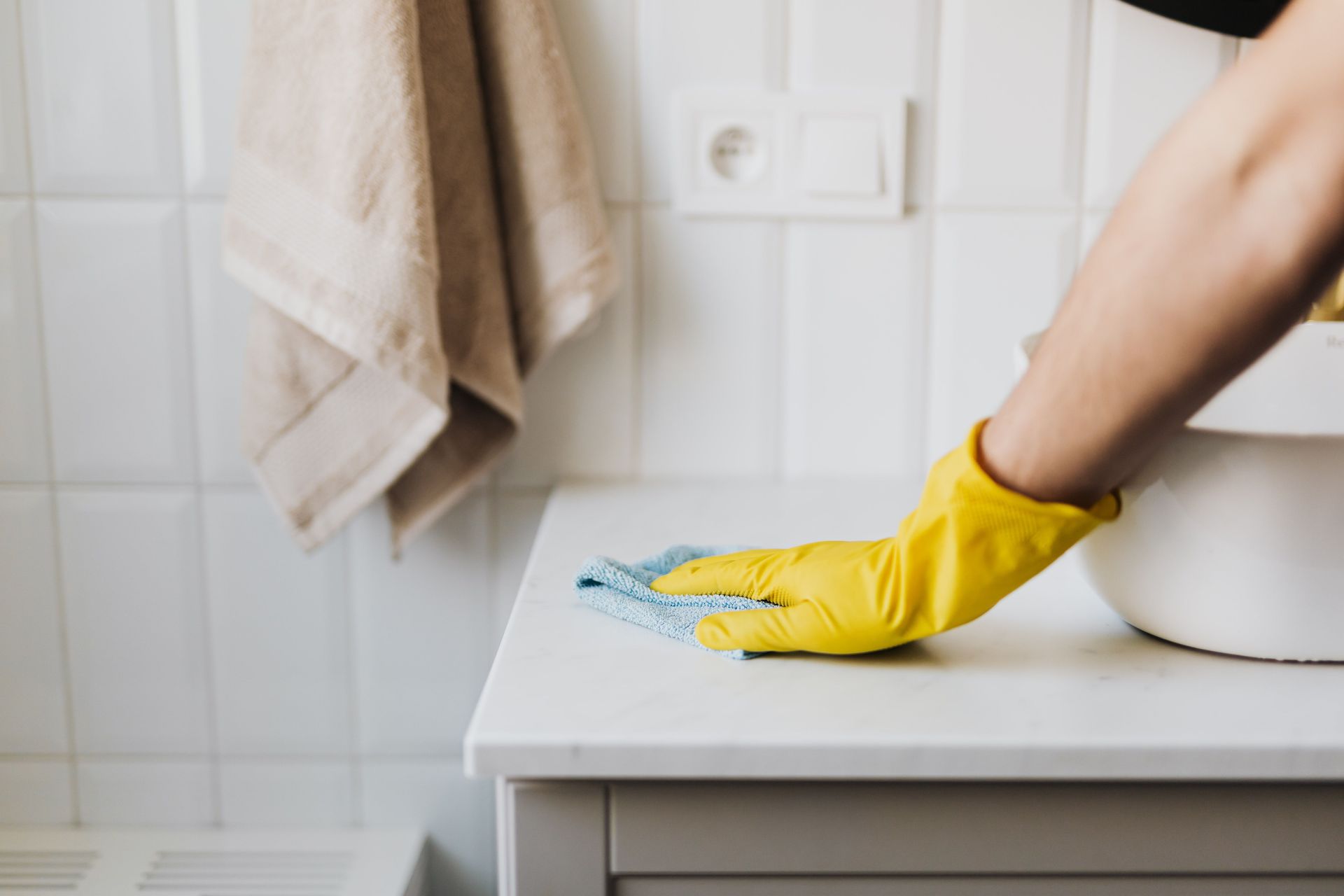 Crop anonymous woman in yellow protective gloves cleaning surface of cabinet near sink in bathroom during housework